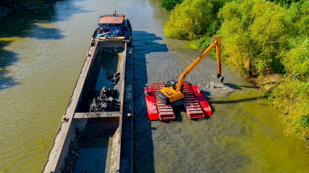 Above view on excavator dredge is dredging, working on river, canal, deepening and removing sediment, mud from riverbed in a polluted waterway.